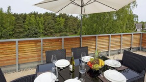 Un espace de restauration en plein air avec une table dressée pour quatre personnes, entourée de chaises en osier, sous un grand parasol.