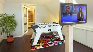 Une pièce avec une table de baby-foot, un téléviseur fixé au mur et une plante en pot.