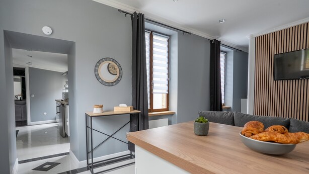 A modern kitchen with a wooden countertop, a bowl of croissants, and a grey wall with a clock.