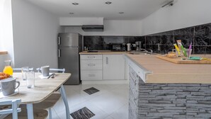 Een moderne keuken met een inbouwoven, magnetron en koffiezetapparaat. Er staat een eettafel met stoelen en een ontbijtje klaar.