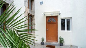 Een gebouw met een houten deur, een klein raam en twee potten met planten op de grond.