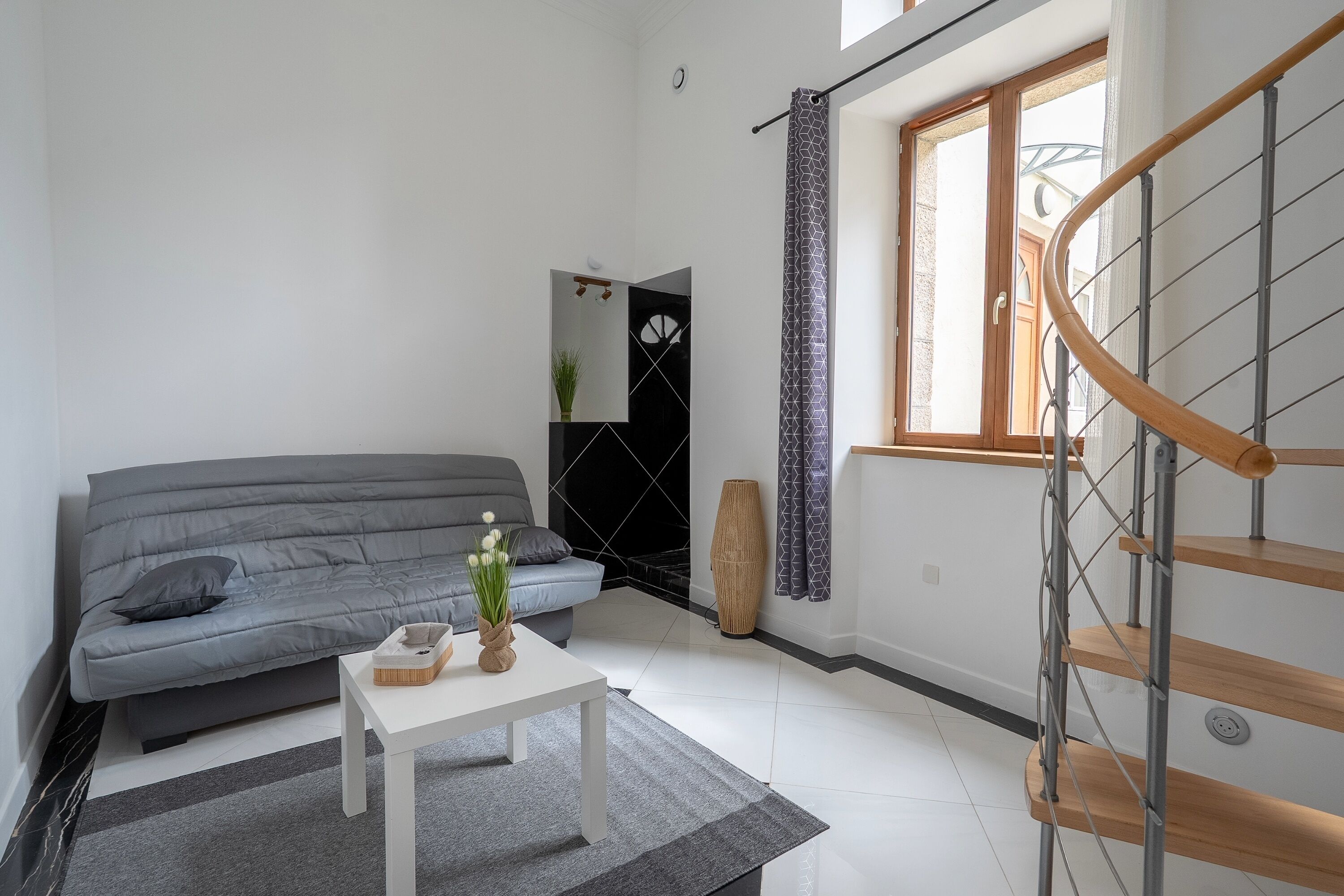 Un salon moderne avec un canapé gris, une table basse blanche et un escalier doté de rampes en bois.