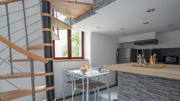 Een moderne keuken met een centraal eiland, een eethoek met een tafel en stoelen, en een wenteltrap.