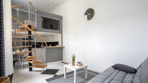 Een moderne woonkamer met een grijze bank, een witte salontafel, een klein plantje en een trap die naar een keuken leidt.