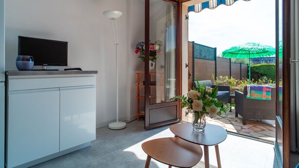 A modern kitchen with a flat-screen TV, a dining table with chairs, and a sliding glass door leading to an outdoor patio with wicker furniture and a green umbrella.