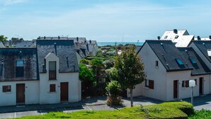 A row of white buildings with dark roofs, arranged in a narrow street with a small tree in the foreground.