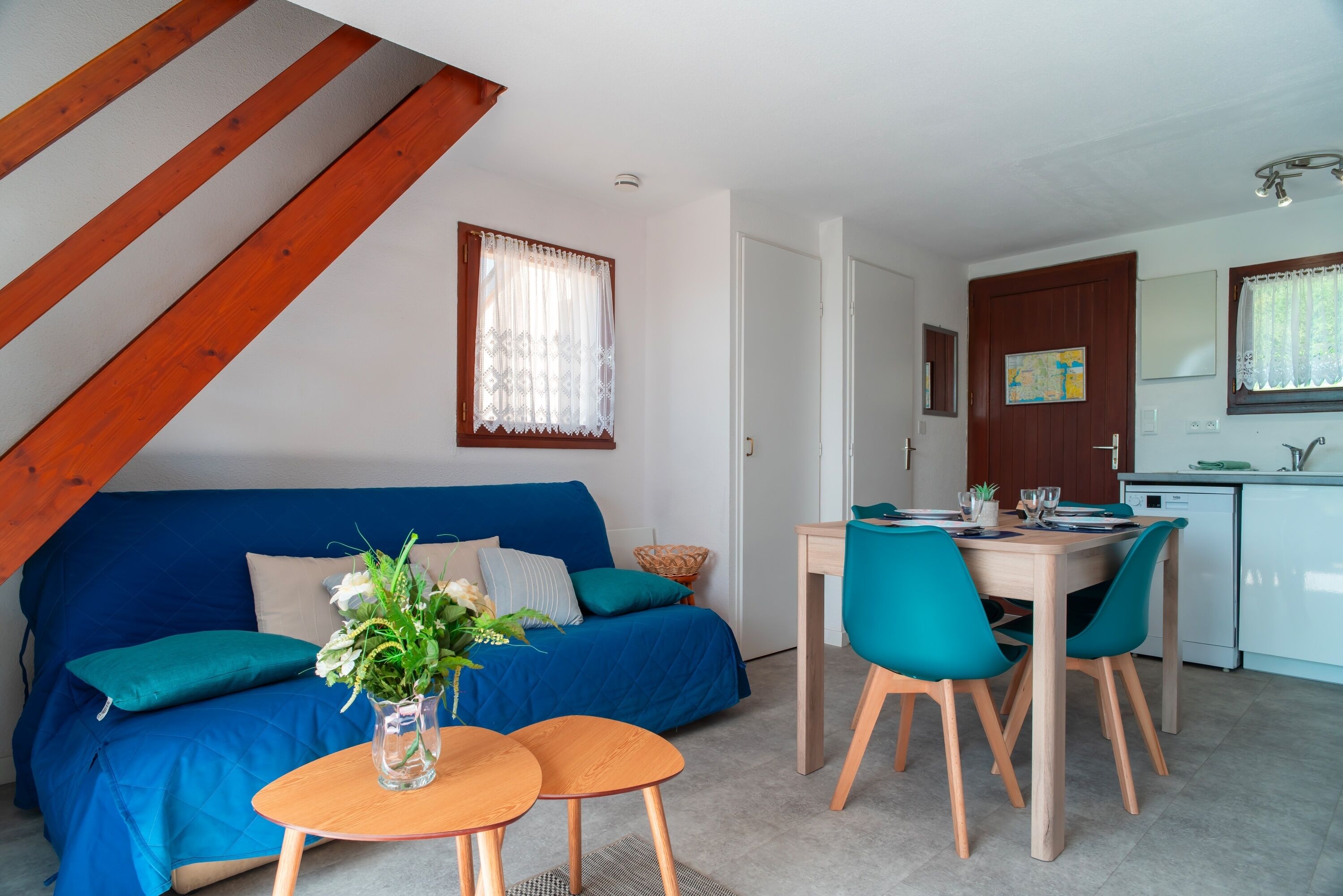 Un espacio habitable moderno con un sofá azul, una mesa de comedor de madera y sillas color turquesa.