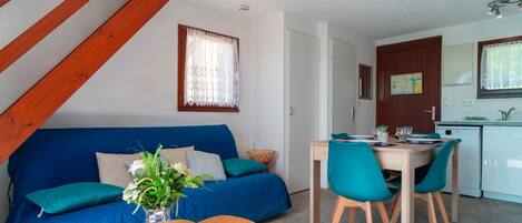 Un espacio habitable moderno con un sofá azul, una mesa de comedor de madera y sillas color turquesa.
