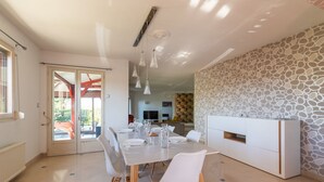 Un espace repas moderne avec une table blanche dressée pour quatre personnes, des chaises transparentes et un meuble blanc intégrant un téléviseur.