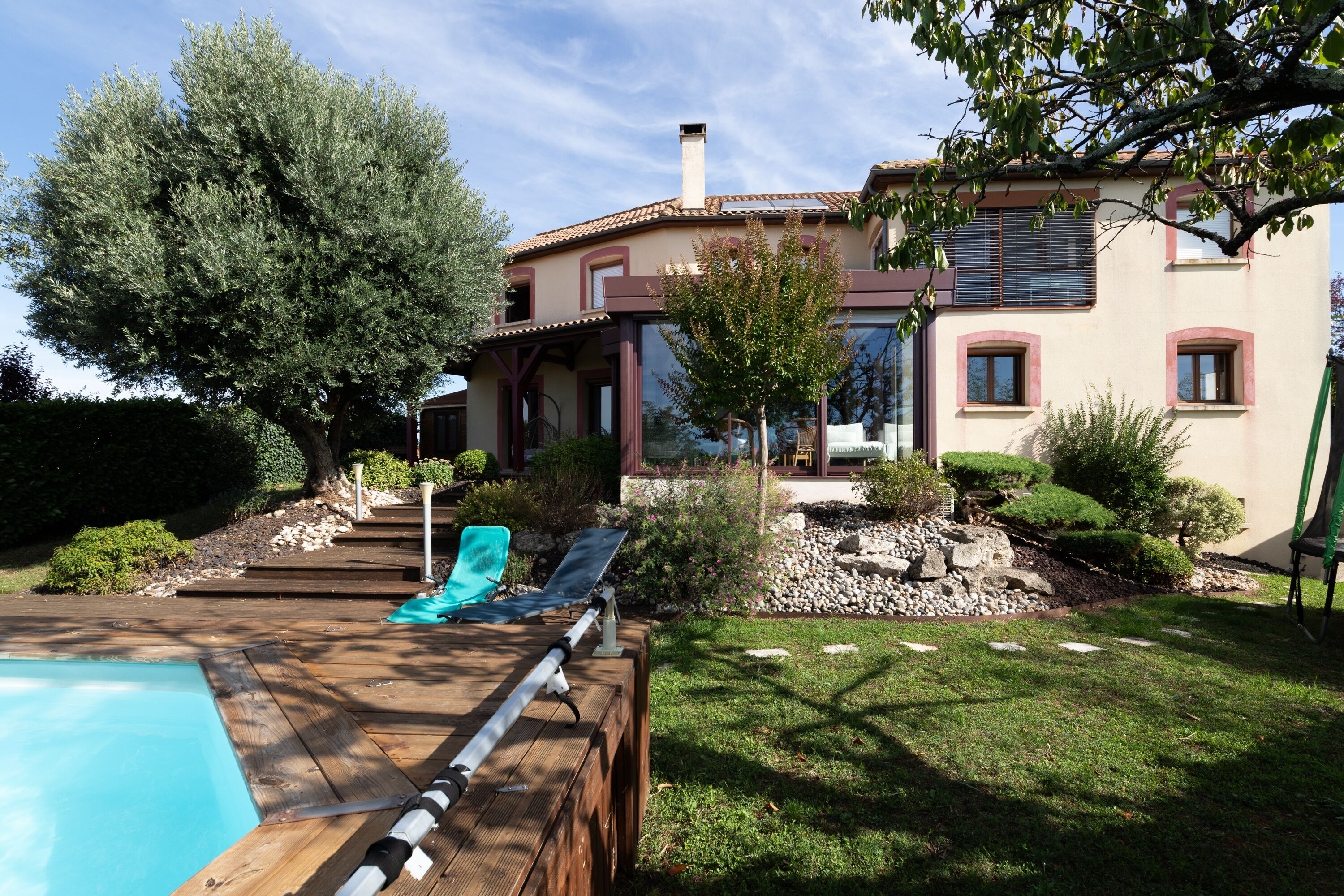 Un espace aménagé au bord de la piscine, avec une terrasse en bois, une chaise longue et une petite piscine.