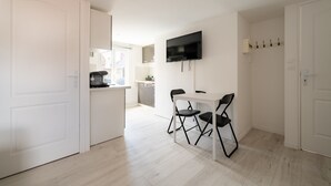 A modern kitchen with white cabinets, a built-in oven, and a dining area with a white table and two black chairs. - Le Nid du Beffroi - Studio centre Doullens (Doullens)