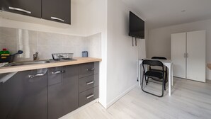 A modern kitchen with dark cabinets, a wooden countertop, and a built-in sink. A black chair is placed at a small dining table. - Le Nid du Beffroi - Studio centre Doullens (Doullens)