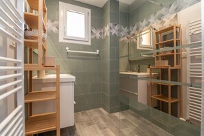 Ein modernes Badezimmer mit Duschkabine aus Glas, Holzregalen und einem integriertem Waschbecken.