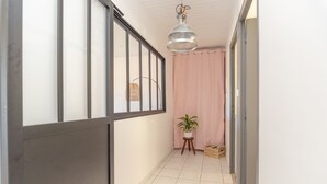 A corridor with a tiled floor, a potted plant, a hanging light fixture, and a pink curtain. - Le gite de la petite famille - proche lacs (Cornod)