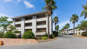 A multi-story building with balconies, surrounded by palm trees and greenery.