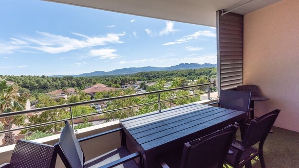 A balcony with a table and chairs, offering a view of a residential area and mountains.
