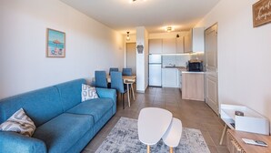 A modern living room with a blue sofa, a dining area with blue chairs, and a kitchen with white cabinets.