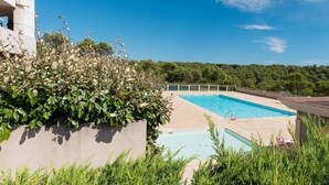 A swimming pool with a clear blue sky, surrounded by greenery and a building.