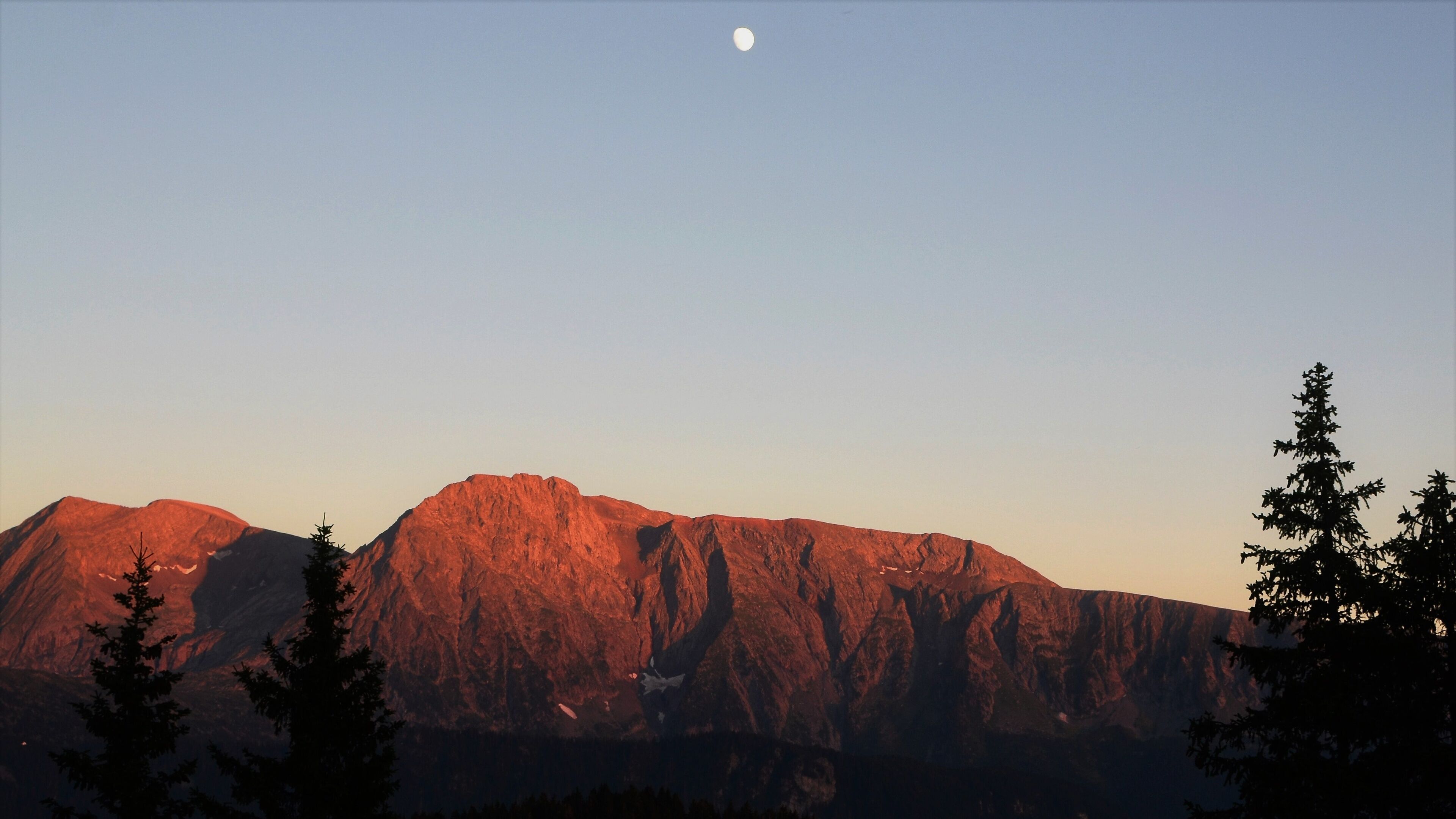 A mountain range with a clear sky and a visible moon.