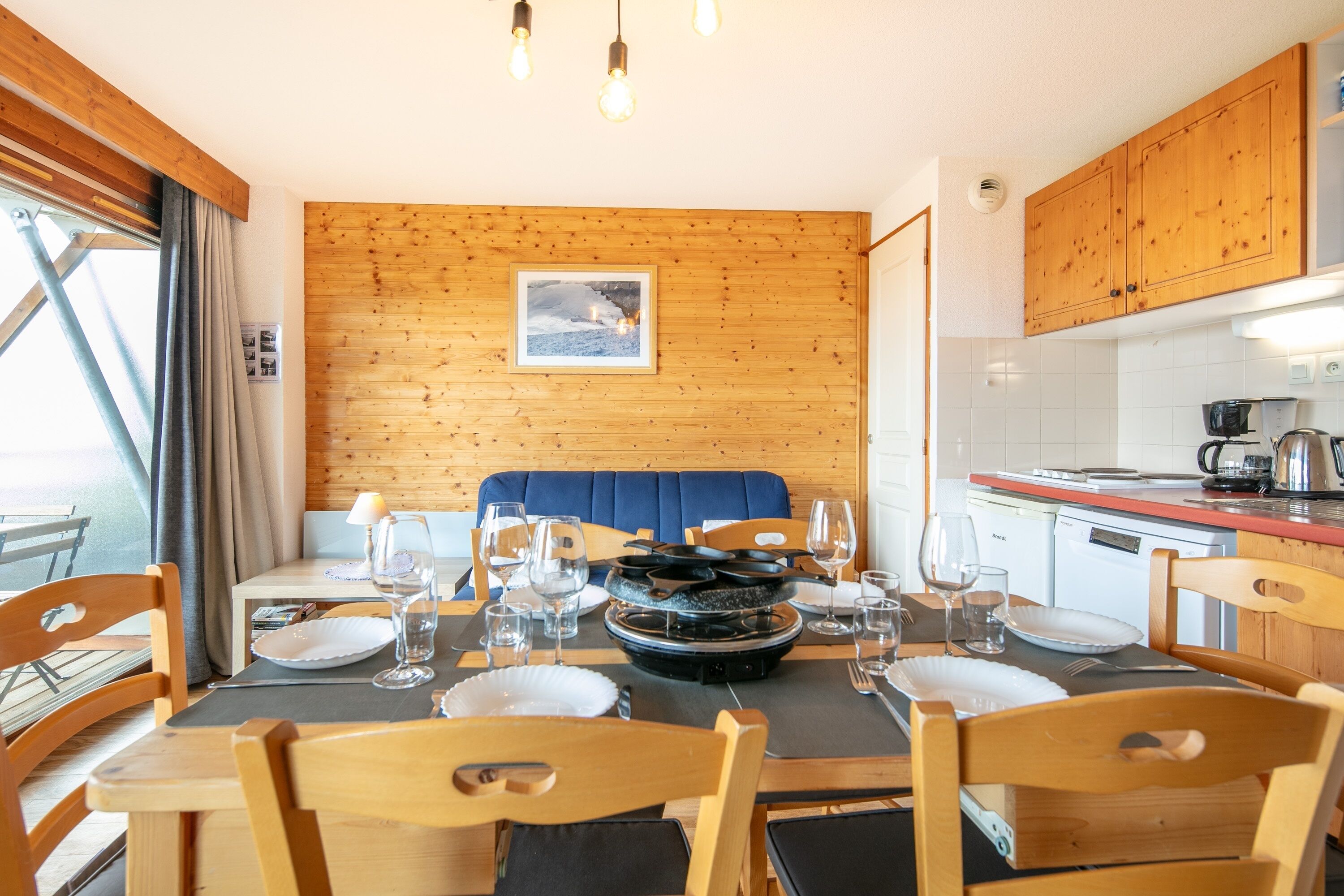 A dining area with a wooden wall, a blue booth, and a kitchen in the background.