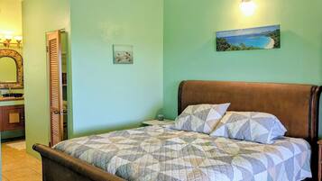 A bedroom with a bed, a ceiling fan, a painting, and a bathroom visible through an open door.