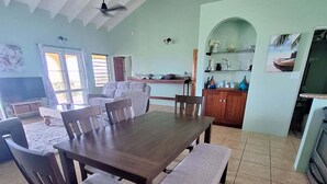 Ein großzügiger Essbereich mit einem großen Holztisch, gepolsterten Stühlen, einem Deckenventilator und einer Küchenzeile mit Arbeitsplatte und Schränken.