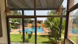 A dining area with a table set for four, overlooking a swimming pool and garden. - Dar mimosa (Sidi Kaouki)