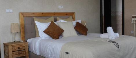Un dormitorio con cabecera de madera, cama con ropa de cama blanca y marrón, una mesita de noche de madera y una toalla blanca sobre la cama.