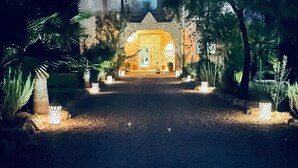A stone building with a central entrance, surrounded by trees and illuminated by ground lights. - Dar mimosa (Sidi Kaouki)