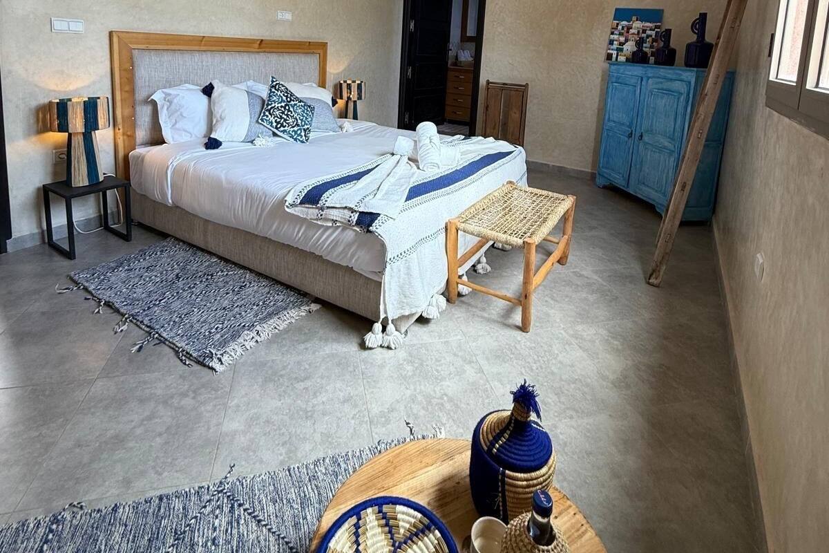 A bedroom with a bed, bedside tables, a wooden bench, a small table with a woven mat, a decorative item, and a wardrobe.