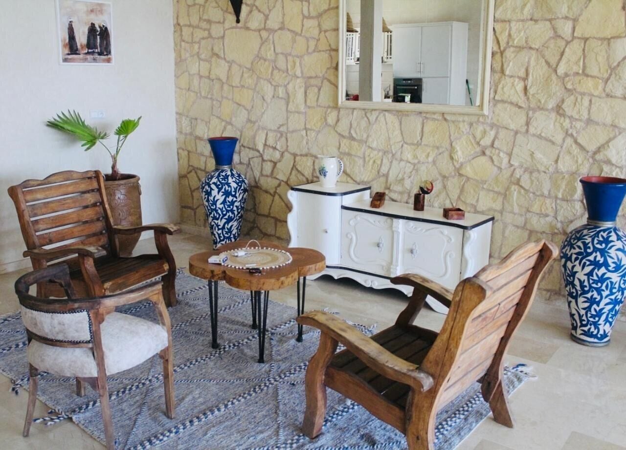 A room with a stone wall, a wooden chair, a small round table, a white cabinet, and two blue vases.
