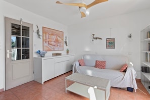 Un salon moderne avec un canapé blanc, une table basse, un ventilateur de plafond, une bibliothèque et un tableau accroché au mur.