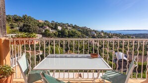 A balcony with a table and chairs, overlooking a hillside with houses.