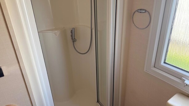A bathroom with a glass shower enclosure, a toilet, and a window with a view of greenery outside. - 2 Bedroom Caravan Sleeps 6 -free Parking -Tv -wifi (Skegness)