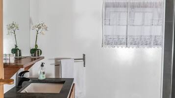 Une salle de bain avec un meuble-lavabo en bois, un lavabo, un bidet et une fenêtre ornée de rideaux en dentelle.