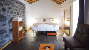 Una camera da letto con un letto, uno scaffale in legno con asciugamani, un tavolino in legno con un telecomando e un bicchiere d'acqua, e un divano in pelle.