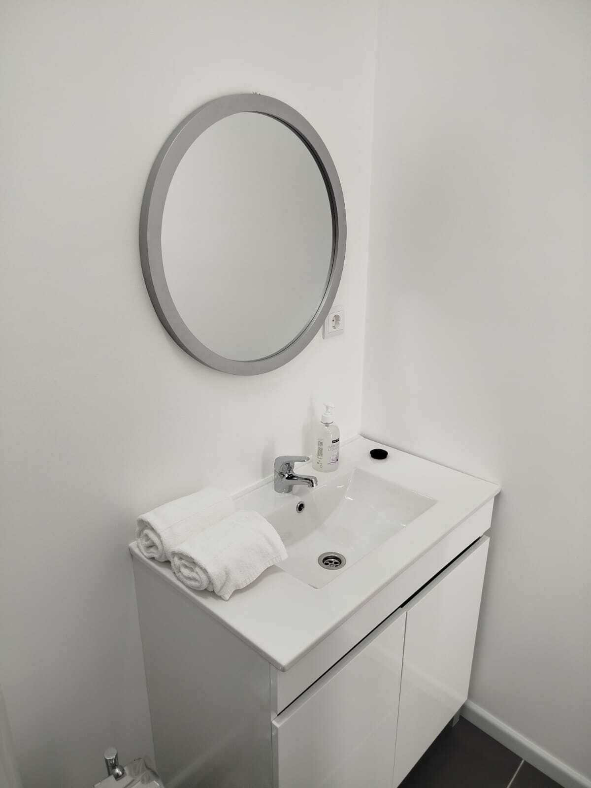 Un baño moderno con un lavabo blanco, un espejo redondo y una toalla en la encimera.