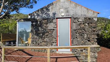 Un edificio de piedra con puerta roja, una ventana pequeña y una valla de madera al frente.