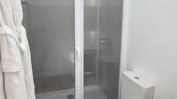 A bathroom with a glass-enclosed shower, a toilet, and a white bathtub.