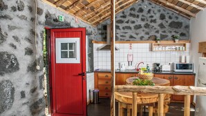 Una cucina rustica con una porta rossa, pareti in pietra, soffitto in legno e un tavolo rotondo in legno con sedie.