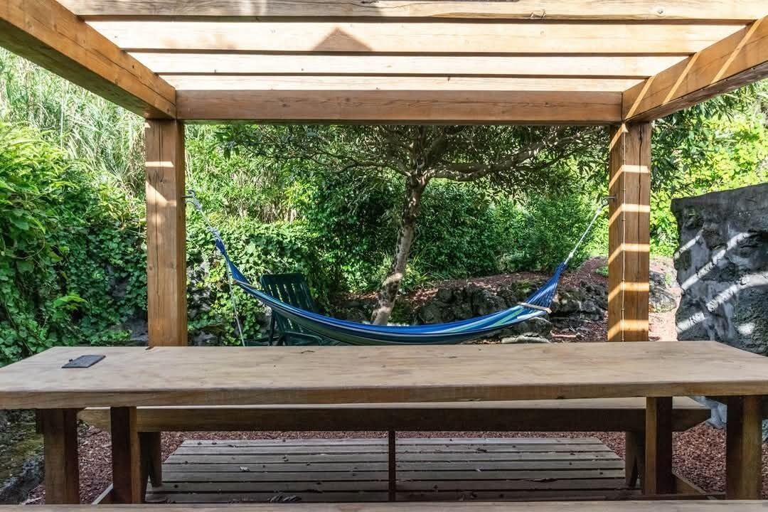 A wooden pergola with a hammock and a table.