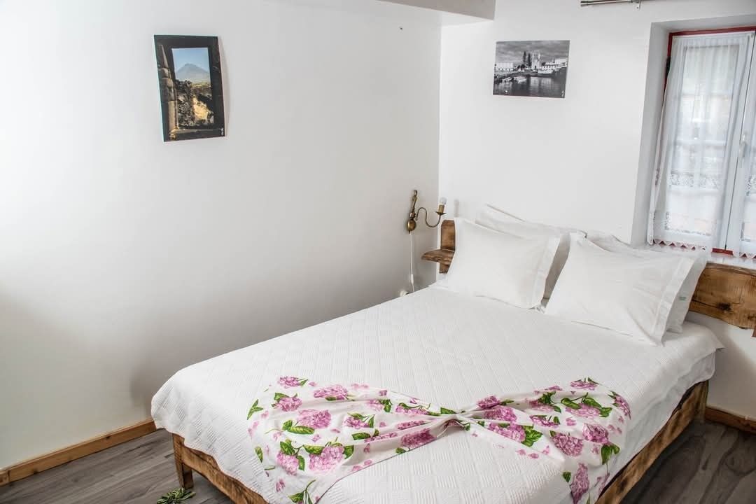 Camera da letto con struttura del letto in legno, biancheria bianca e coperta a motivi floreali.