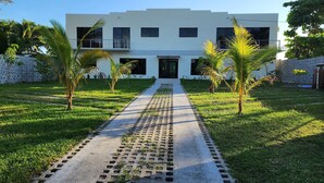 A modern building with a central entrance, surrounded by a well-maintained lawn and palm trees.
