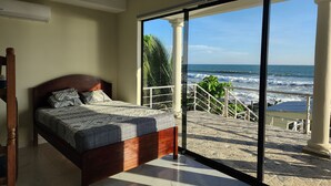 A bedroom with a large bed, a view of the ocean through a sliding glass door, and a staircase leading to a balcony.