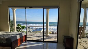 A bedroom with a large sliding glass door leading to a balcony with a view of the ocean.