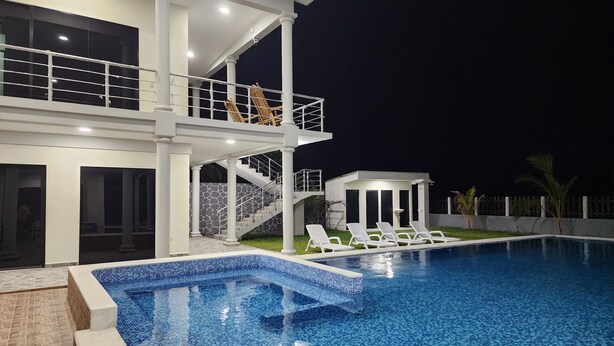 A two-story house with a swimming pool, outdoor seating, and a small gazebo.
