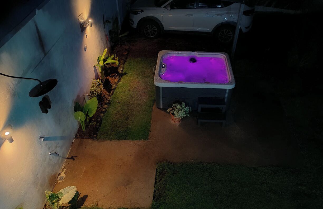 Un jardín trasero con un jacuzzi, un coche blanco y un aplique de pared.