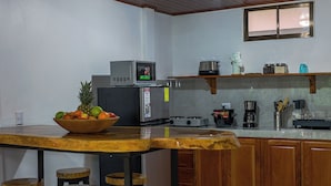 A kitchen with a wooden table, stools, a microwave, a stove, and various kitchen items.