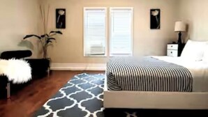 A bedroom with a bed, bedside tables, a lamp, a window with blinds, and a decorative rug. - Grand View | Walk to Falls, Casino & Attractions (Niagara Falls)