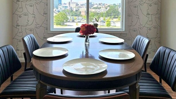 A dining room with a round table set for six, chairs, and a vase with flowers. - Grand View | Walk to Falls, Casino & Attractions (Niagara Falls)
